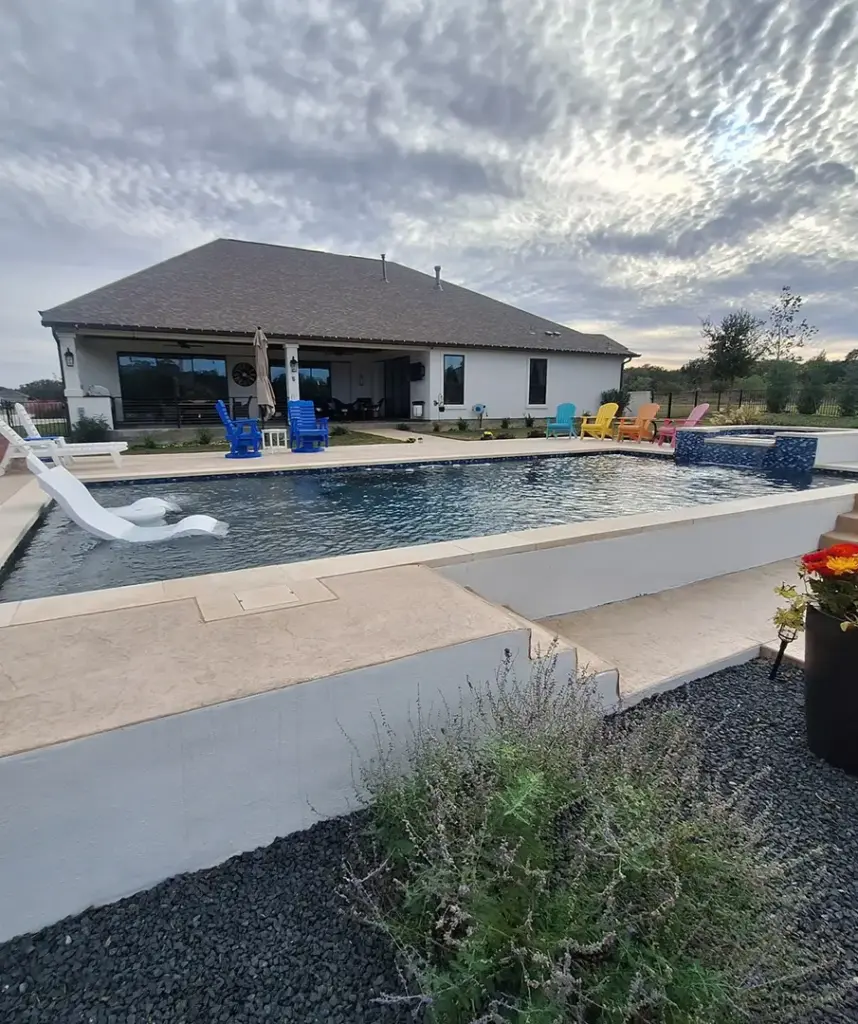 Custom backyard pool with a raised spa and white loungers.